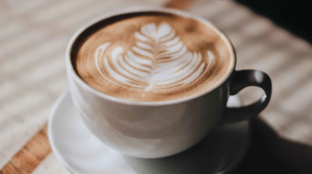 Coffee cup filling with espresso and steamed milk beneath a modern office coffee machine.