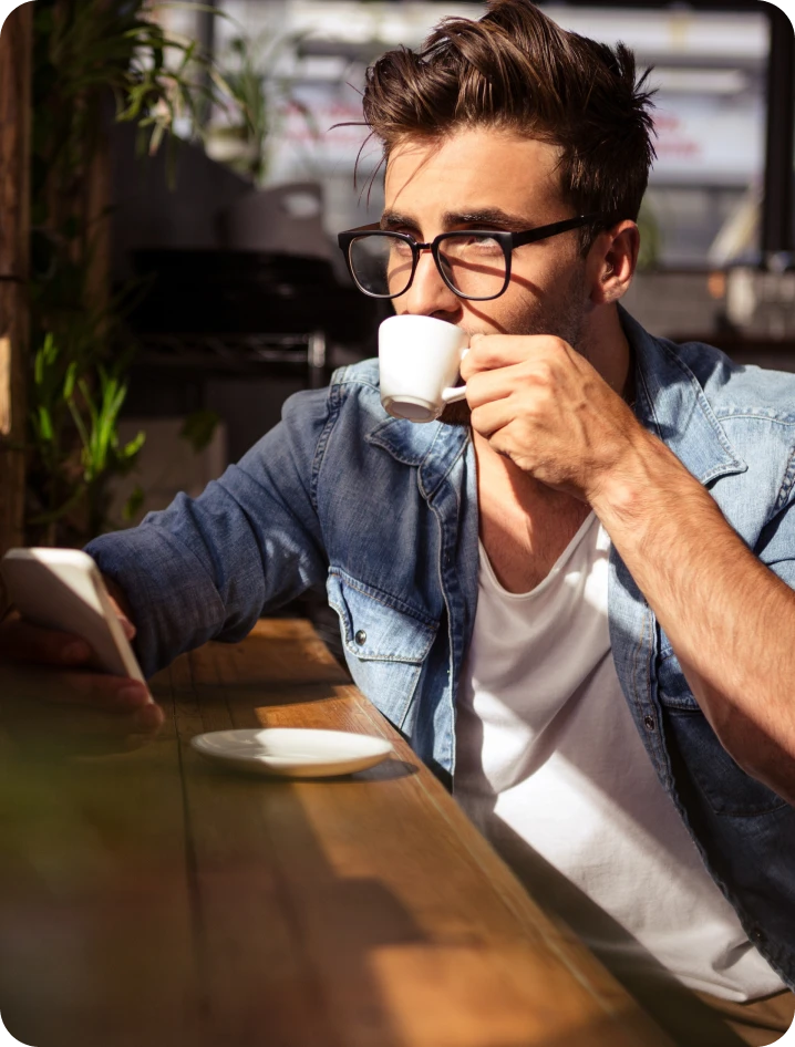 A person sips on a cup of espresso while looking at their phone at an outdoor coffee shop.